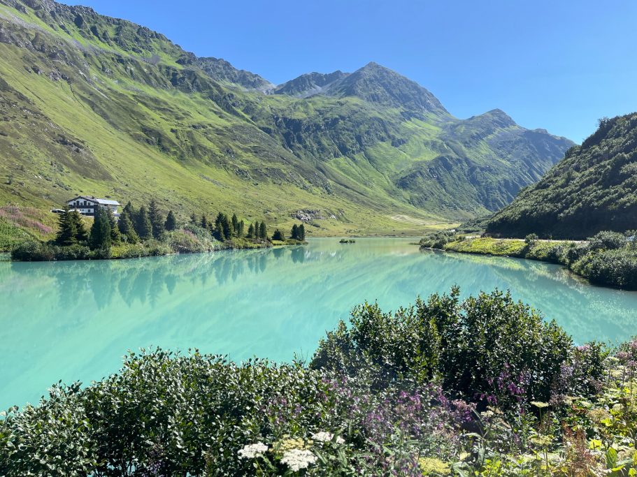 Stausee Kops Blick auf einen klaren, türkisfarbenen See, umgeben von grünen Bergen und flora.