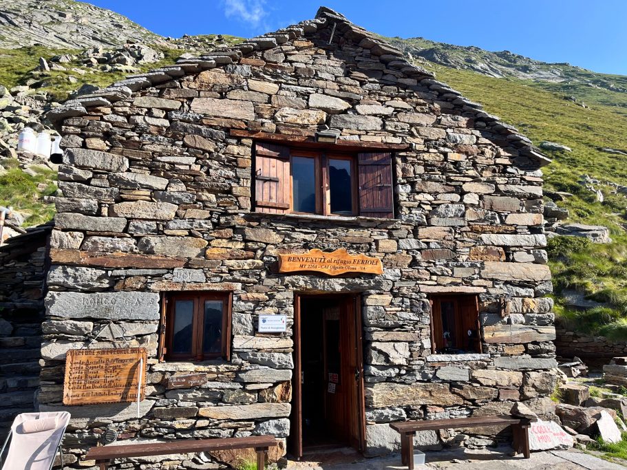 Rifugio Santino Ferioli Altes Steinhaus mit Holzfenster und Eingang, umgeben von Bergen und blauem Himmel.