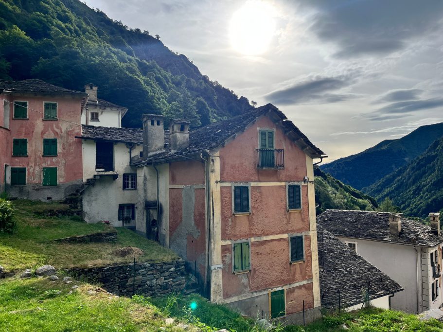 Campello Monti Verlassene Häuser in den Bergen, umgeben von grüner Landschaft und einem bewölkten Himmel.