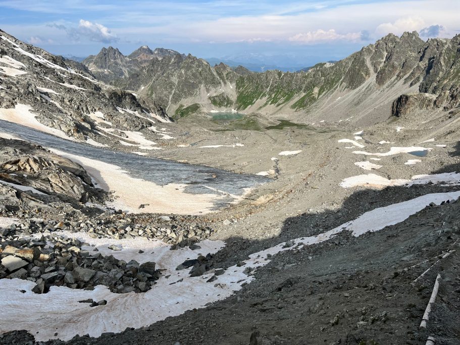 Seegletscher Berglandschaft mit Gletscherresten und steilen Felsen, umgeben von grünen Hügeln.