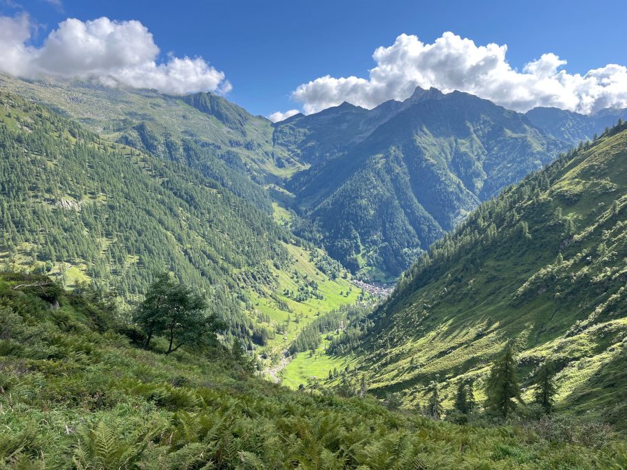 Blick ins Tal mit grünen Hügeln und Bergen unter einem blauen Himmel mit Wolken.