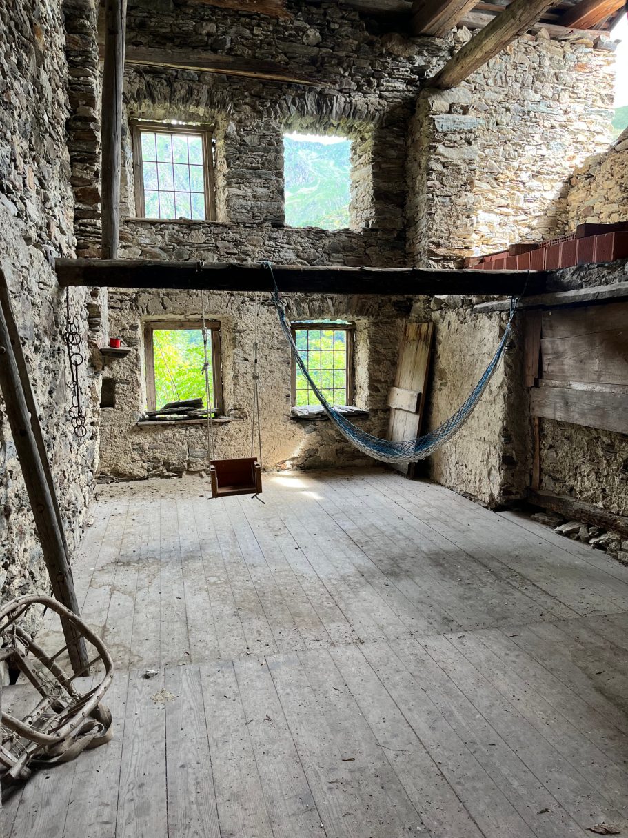 Verlassener Raum mit Steinwänden, Holzfußboden und einer Hängematte zwischen den Wänden.