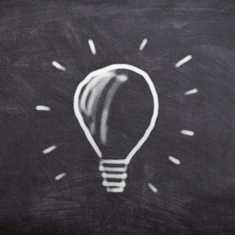 Glühbirne mit Strahlen auf einer Tafel skizziert.