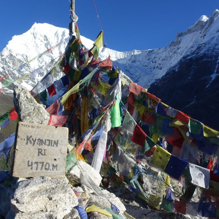 Bunt gefärbte Gebetsfahnen und ein Schild auf einem Berggipfel in den Himalayas.