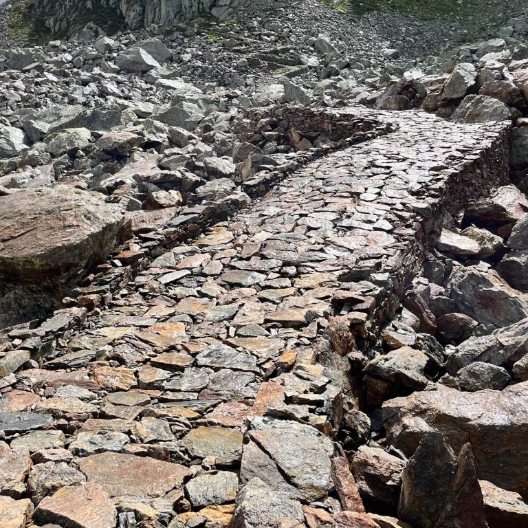 Ein gepflasterter Weg zwischen Steinen in unebenem Gelände.