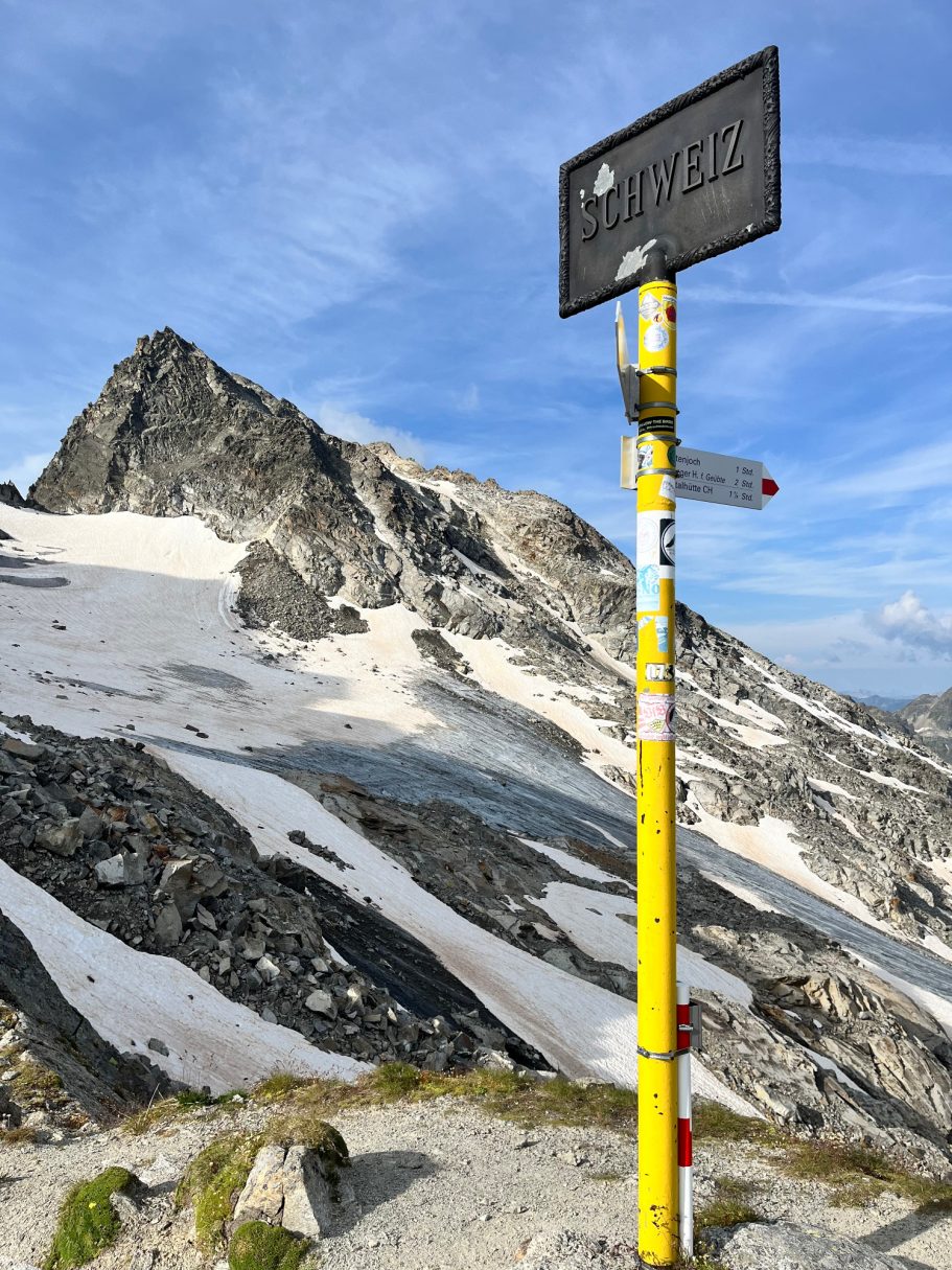 Seelücke Berglandschaft mit einem gelben Wegweiser und schneebedeckten Gipfeln im Hintergrund.