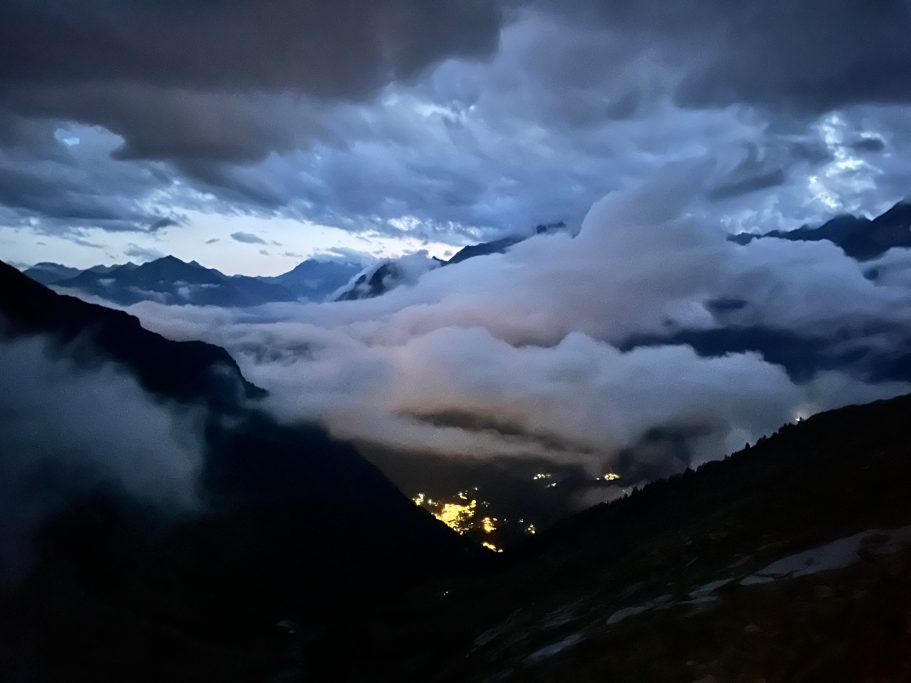 Alagna Nachtaufnahme von Bergen mit Wolken und einem leuchtenden Tal unter dem Nebel.