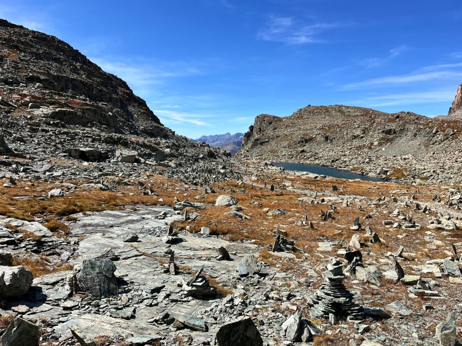 Monviso Berglandschaft mit felsigem Terrain und einem kleinen See im Hintergrund unter blauem Himmel.