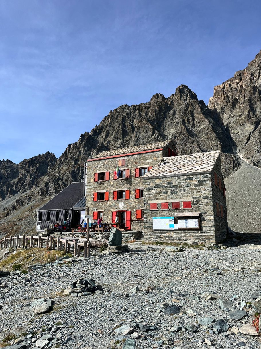 Rifugio Quintino Sella Bergbauernhaus aus Stein mit roten Fensterläden, umgeben von schroffen Felsen.
