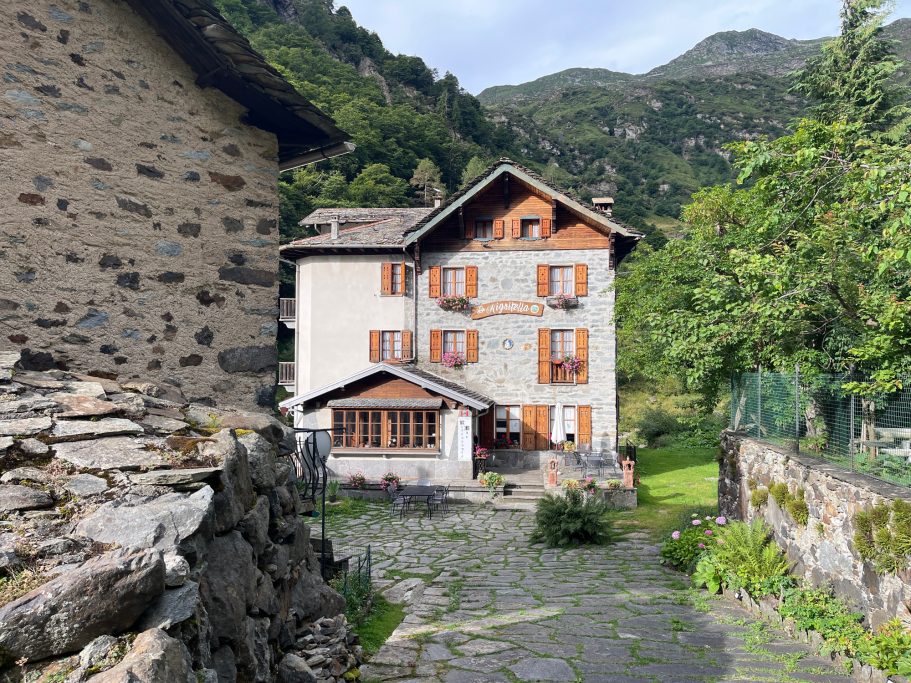 Campello Monti Zwei Gebäude in der Natur mit Bergen im Hintergrund und einem klaren Himmel.