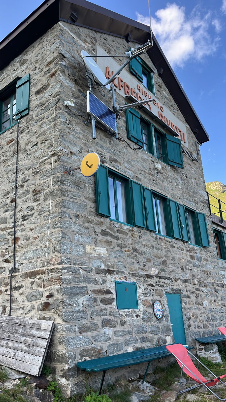 Rifugio Alfredo Rivetti Steinernes Gebäude mit grünen Fensterläden und Satellitenschüssel, umgeben von Natur.