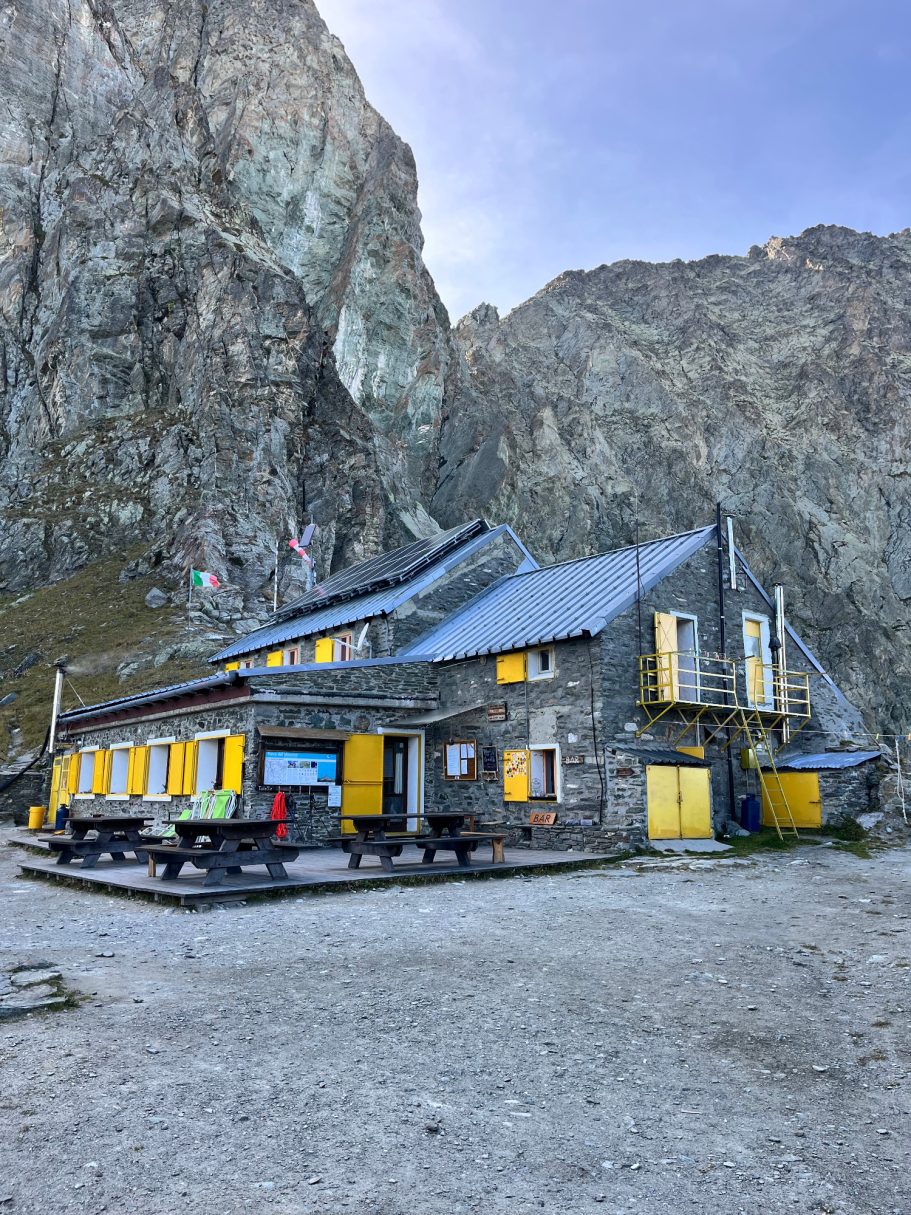Rifugio Giacoletti Bergstützpunkt aus Holz mit gelben Fenstern, umgeben von steilen Felsen und Bergen.